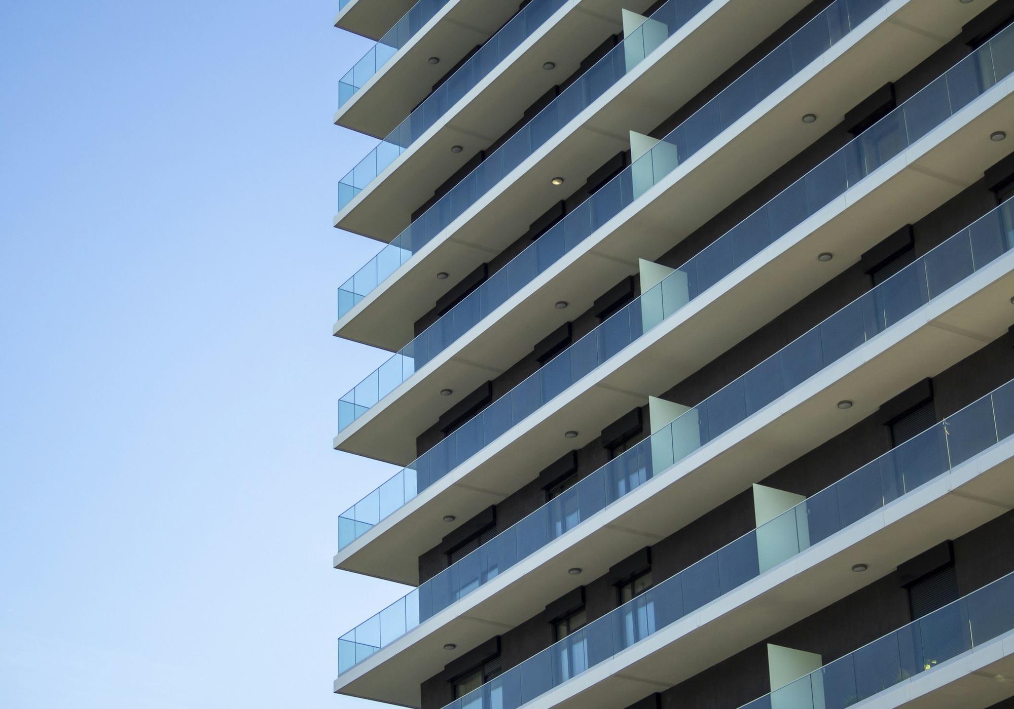 Moderne Wohnhausfassade mit Glasbalkonen vor blauem Himmel